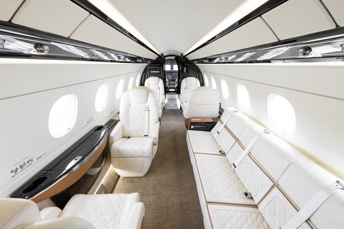 The luxurious white and brown interior of a private jet cabin with quilted seats and a long sofa.